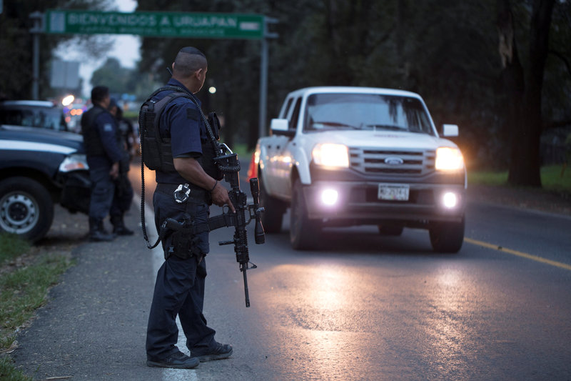 Police officers stand guard as they carry out inspections at a checkpoint after 13 people were killed in battles between rival gangs in two states in central and western Mexico, in Uruapan