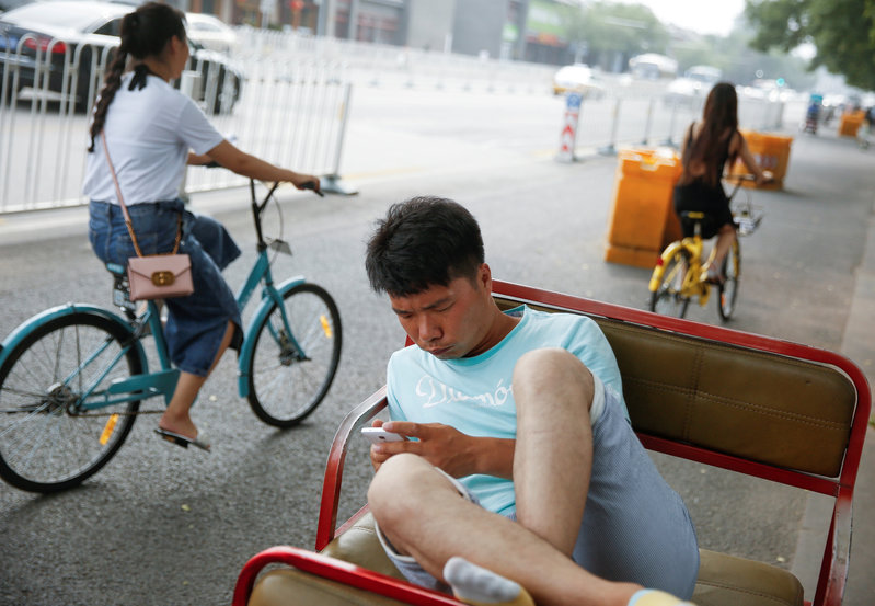 FILE PHOTO: A electric rickshaw driver uses a mobile phone as he takes a break in Beijing