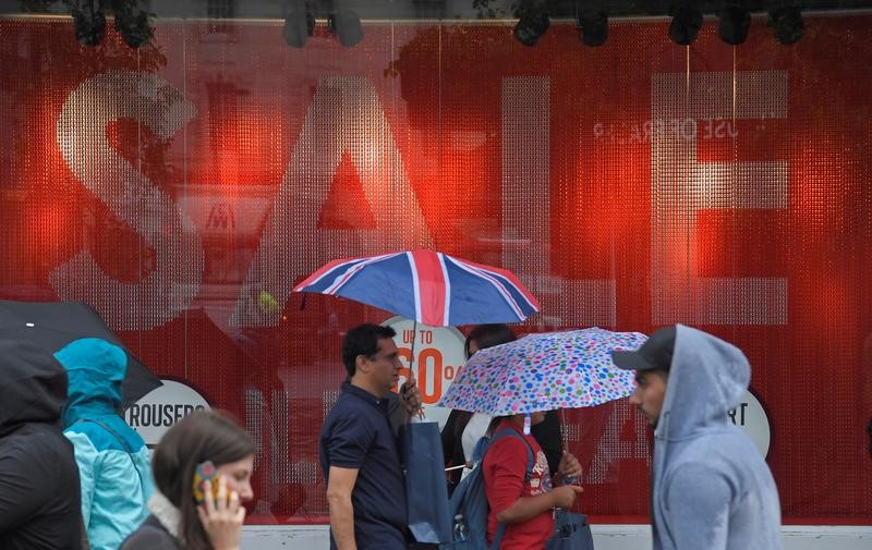 FILE PHOTO: Shoppers walk past a sale sign in central London
