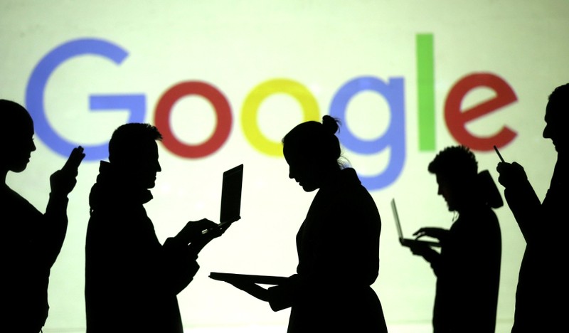 FILE PHOTO: Silhouettes of laptop and mobile device users are seen next to a screen projection of Google logo in this picture illustration