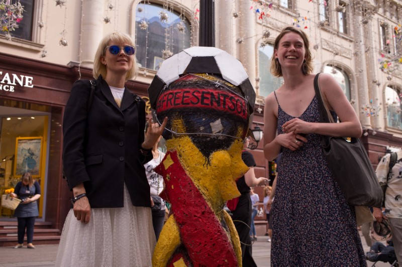 Pedestrians pose near a mock-up World Cup trophy bound in barbed wire and carrying the slogan