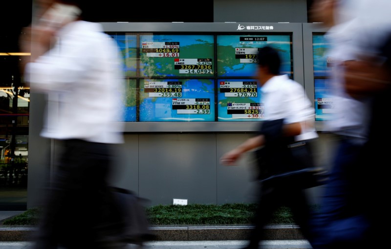 People walk past an electronic board showing Japan's Nikkei average outside a brokerage at a business district in Tokyo