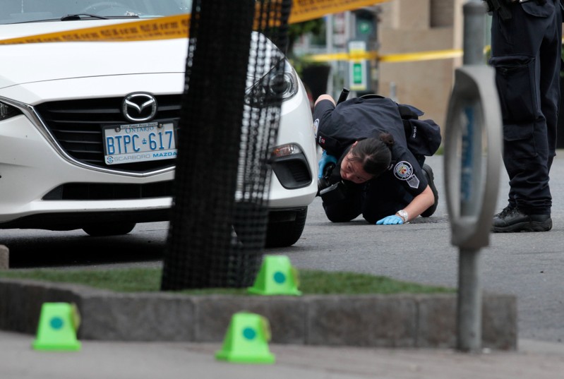 A police officer looks for evidence under a car while investigating a mass shooting in Toronto