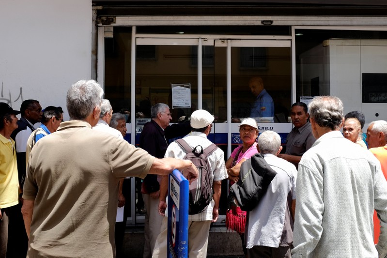 People line up to withdraw a part of their pensions outside a bank branch in Caracas