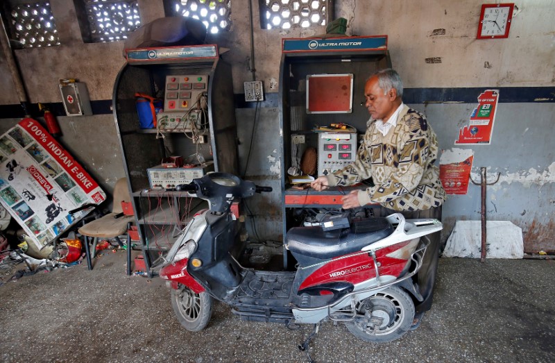 A worker checks the power supply to recharge an electric scooter inside a workshop in Ahmedabad