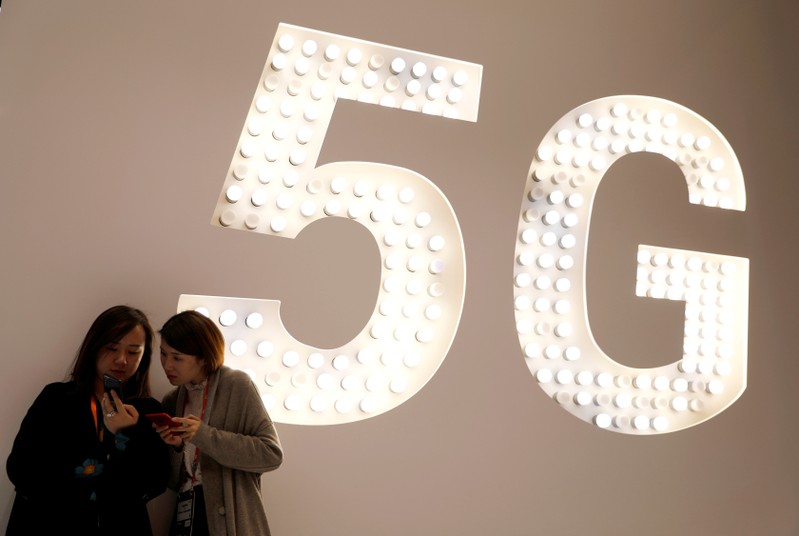 FILE PHOTO: Visitors use their mobiles phones as they stand next to a 5G Led Smart Bulb panel inside the Xiaomi booth at the Mobile World Congress in Barcelona