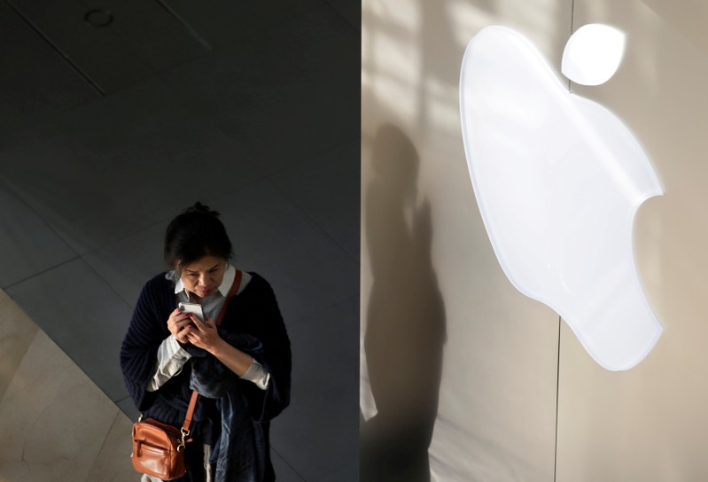 FILE PHOTO: A woman holds her phone near an Apple company logo in Beijing