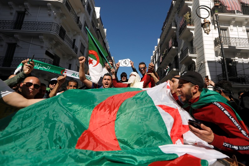People carry their national flags as they protest over President Abdelaziz Bouteflika's decision to postpone elections and extend his fourth term in office, in Algiers
