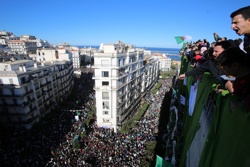 Demonstrators stand atop of a building during a protest over President Abdelaziz Bouteflika's decision to postpone elections and extend his fourth term in office, in Algiers