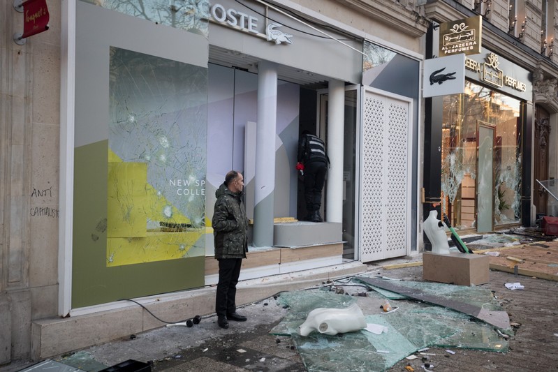 A man stand in front of a damaged shop on the Champs Elysees avenue during a demonstration by the