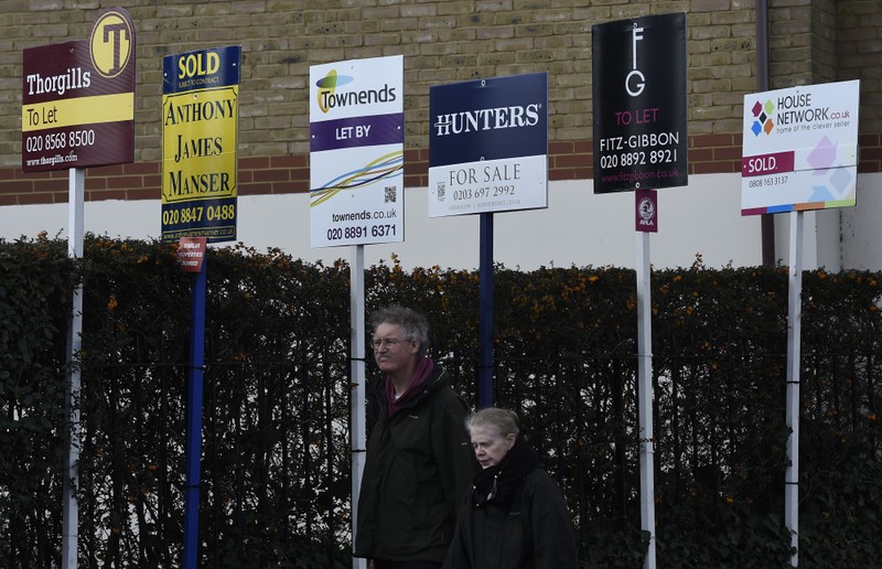 A couple walk past property estate agent sales and letting signs in London, Britain
