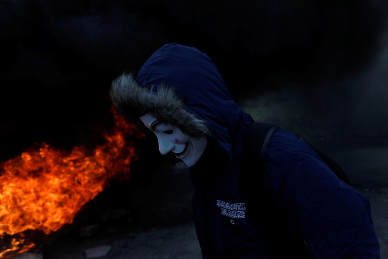 Palestinian demonstrator wearing a mask stands next to a burning tire during clashes with Israeli forces at a protest marking Land Day, near the Jewish settlement of Beit El, in the Israeli-occupied West Bank