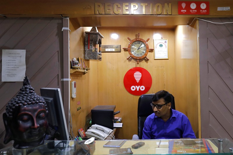 An employee sits next to the logo of OYO, India's largest and fastest-growing hotel chain, at the reception of a hotel in New Delhi