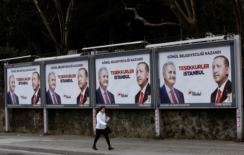 A woman walks past by AK Party billboards with pictures of Turkish President Tayyip Erdogan and mayoral candidate Binali Yildirim in Istanbul