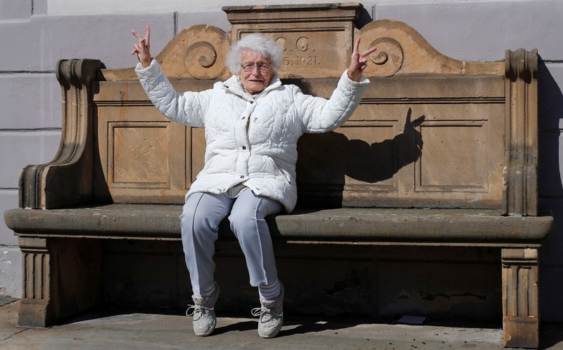Lisel Heise, a 100-year-old former teacher, sits on a stone bench from 1921 and flashes victory signs in front of the townhall in Kirchheimbolanden