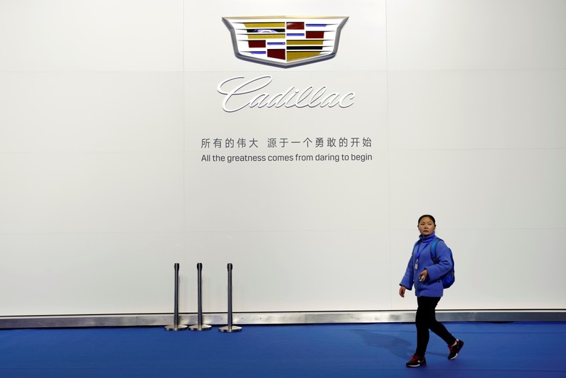 Woman walks past a board with a sign of Cadillac of GM during the media day for Shanghai auto show