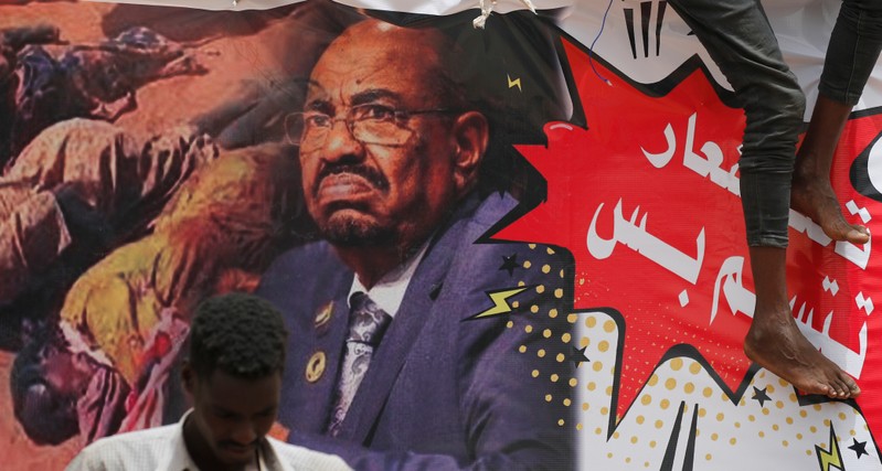 FILE PHOTO - A protester stands in front of a banner depicting former Sudanese President Omar al-Bashir in front of the Defence Ministry in Khartoum