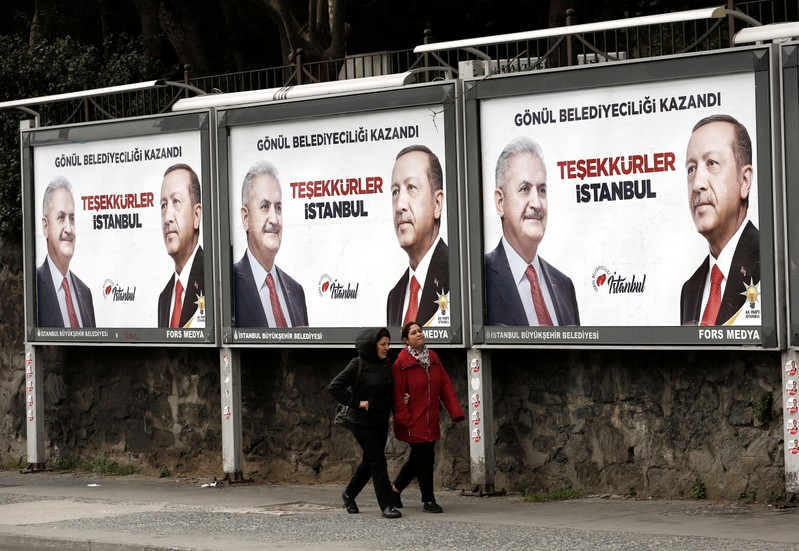 People walk past by AK Party billboards with pictures of Turkish President Tayyip Erdogan and mayoral candidate Binali Yildirim in Istanbul