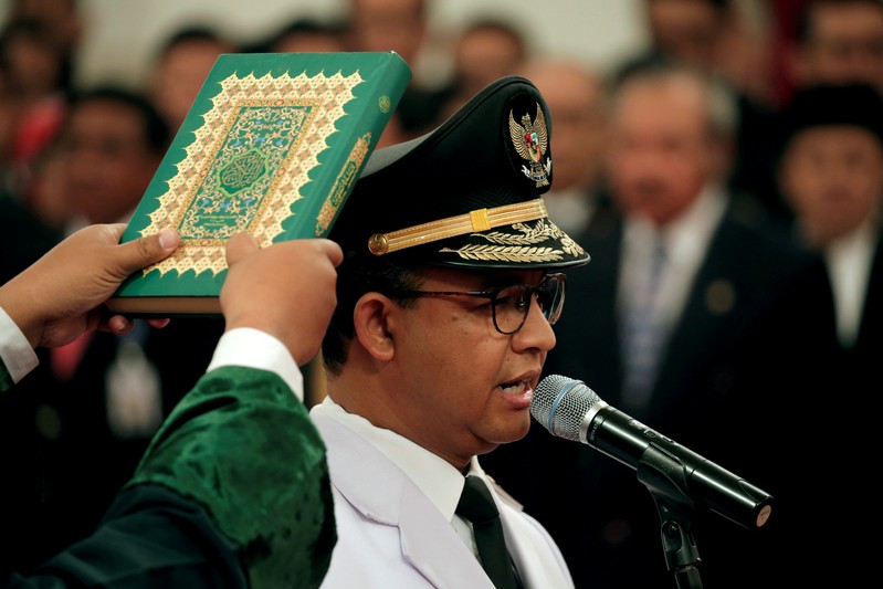 FILE PHOTO: A man holds a Koran as Jakarta Governor Anies Baswedan stands during a swearing-in ceremony at the Presidential Palace in Jakarta