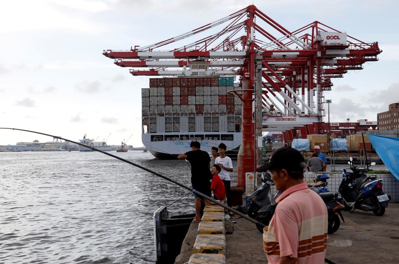 FILE PHOTO: People fish in front of an Orient Overseas Container Line container ship