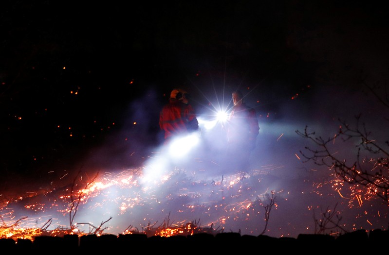 Firefighters tackle a fire on a patch of moorland above the village of Uppermill
