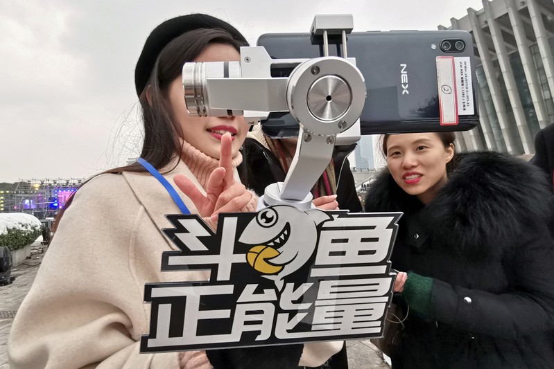 FILE PHOTO: A girl broadcasts live from a phone as she holds a selfie stick with a sign of the live-streaming platform DouYu during an event celebrating the new year in Wuhan