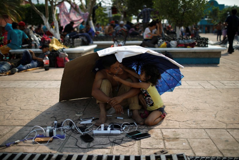 A migrant from Honduras watch other migrants' cellphones as they gather in an improvised shelter during a break in their journey towards the United States, in Escuintla