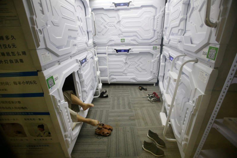 FILE PHOTO: An IT employee takes off shoes as he prepares to sleep in a capsule bed unit at Xiangshui Space in Beijing