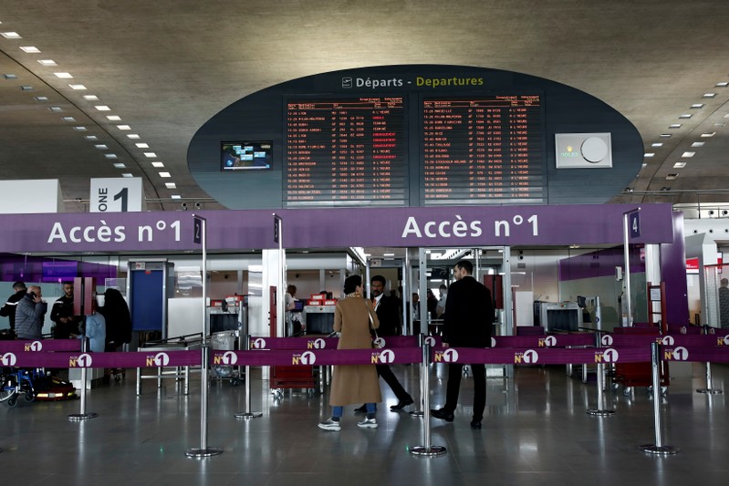 FILE PHOTO: Passengers gather in a departure hall as screens display flight information inside Charles de Gaulle airport, operated by Aeroports de Paris, in Roissy