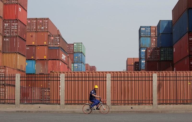 A worker cycles past containers outside a logistics center near Tianjin Port