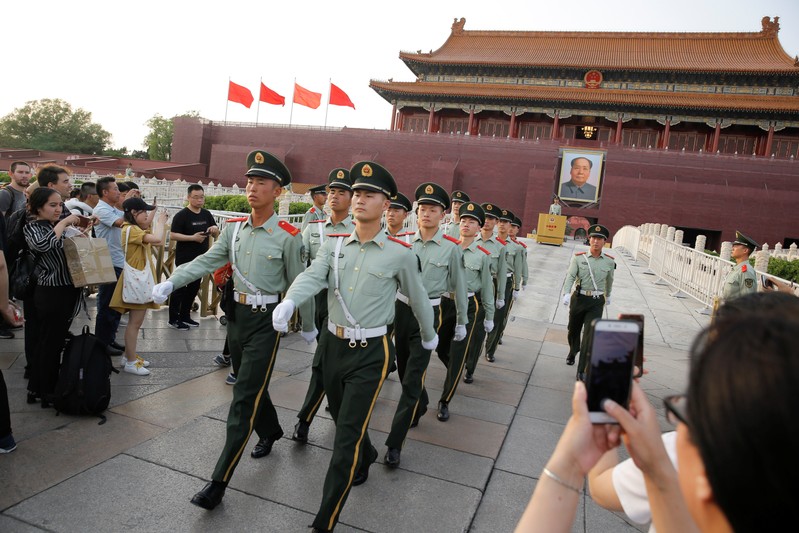 People take pictures of paramilitary officers marching in formation in Tiananmen Square in Beijing