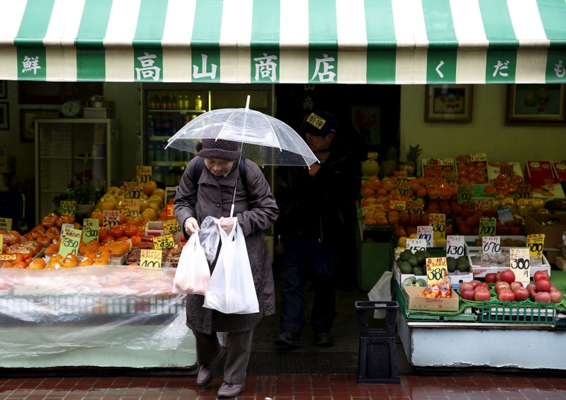 FILE PHOTO: A shopper holding plastic bags walks out from a greengrocer's at Tokyo's Sugamo district, an area popular with the Japanese elderly, in Tokyo
