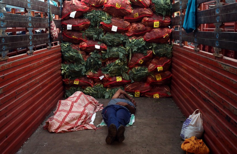 Men sleep in a supply truck loaded with sacks of cauliflower at a vegetable wholesale market in Mumbai