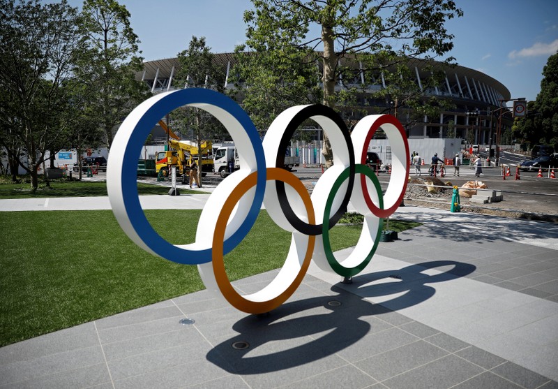 FILE PHOTO: Construction workers and passersby are seen through Olympic rings in front of the construction site of the New National Stadium, in Tokyo