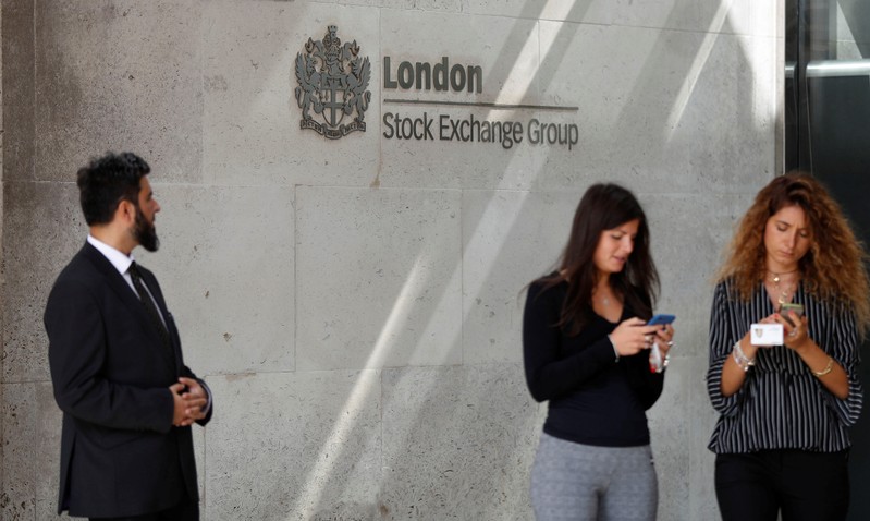 FILE PHOTO: People check their mobile phones as they stand outside the entrance of the London Stock Exchange in London