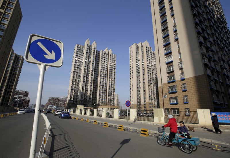FILE PHOTO: A woman rides a tricycle carrying a child near a residential compound in Beijing's Tongzhou district
