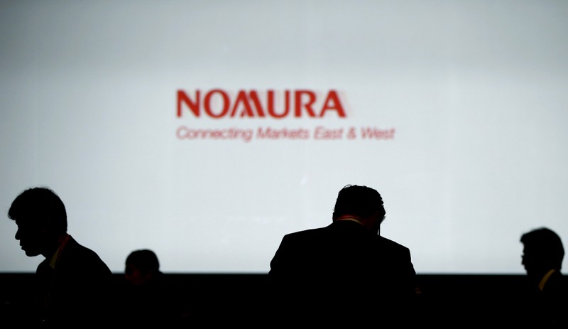FILE PHOTO: Investors stand in front of a screen showing the logo of Nomura Holdings in Tokyo