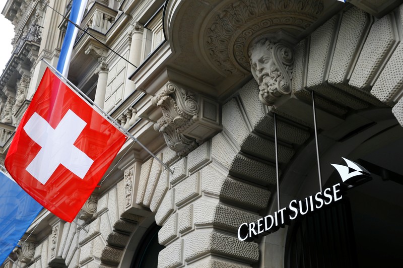 Switzerland's national flag flies beside a logo of Swiss bank Credit Suisse in Zurich