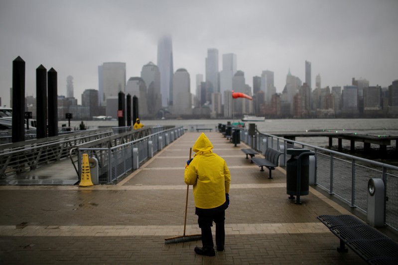 A ferry worker cleans the path for commuters during light snowfall while the New York skyline and the One World Trade Center are seen from Exchange Place