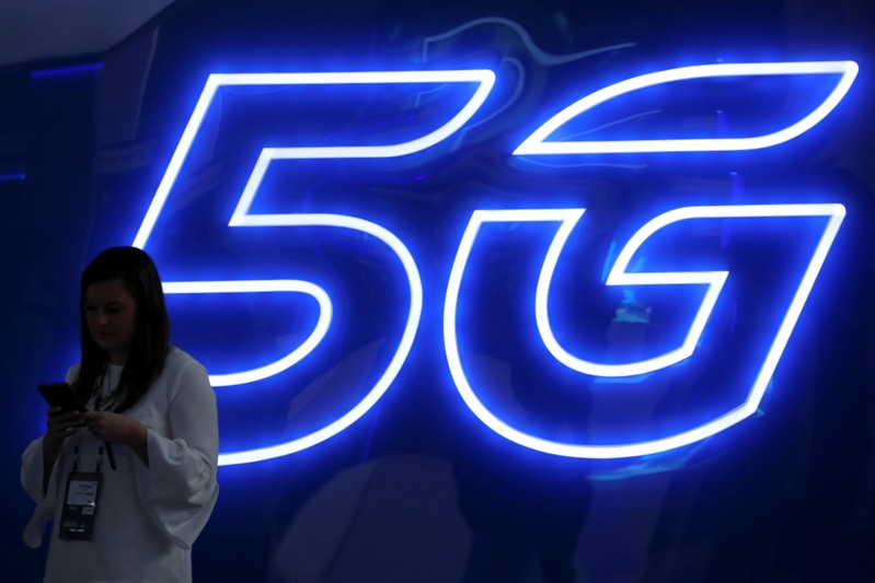 FILE PHOTO: A woman looks at her mobile phone next to a 5G sign at the Mobile World Congress in Barcelona
