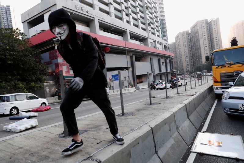A protester stands on the divider as protesters block roads in Wong Tai Sin district, as they call for a general strike, in Hong Kong