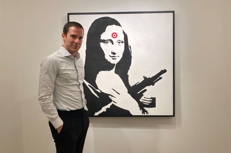Scott Lynn, CEO and founder of Masterworks, poses next to a Banksy artwork in New York