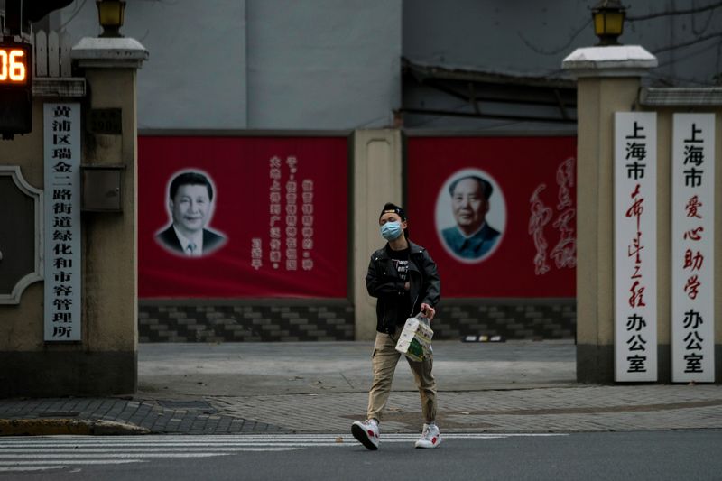 A man wearing a mask walks by portraits of Chinese President Xi Jinping and late Chinese chairman Mao Zedong as the country is hit by an outbreak of the novel coronavirus, on a street in Shanghai