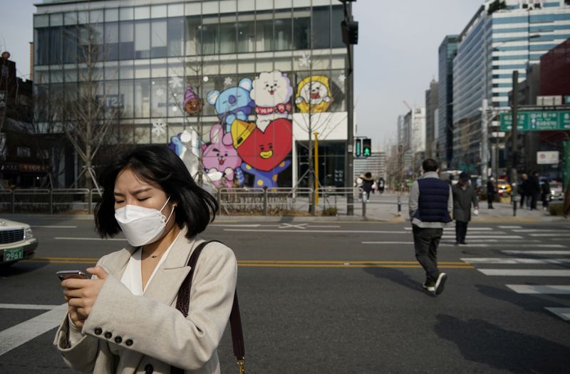 A woman wearing a mask to prevent the coronavirus uses her mobile phone at a shopping district in Seoul