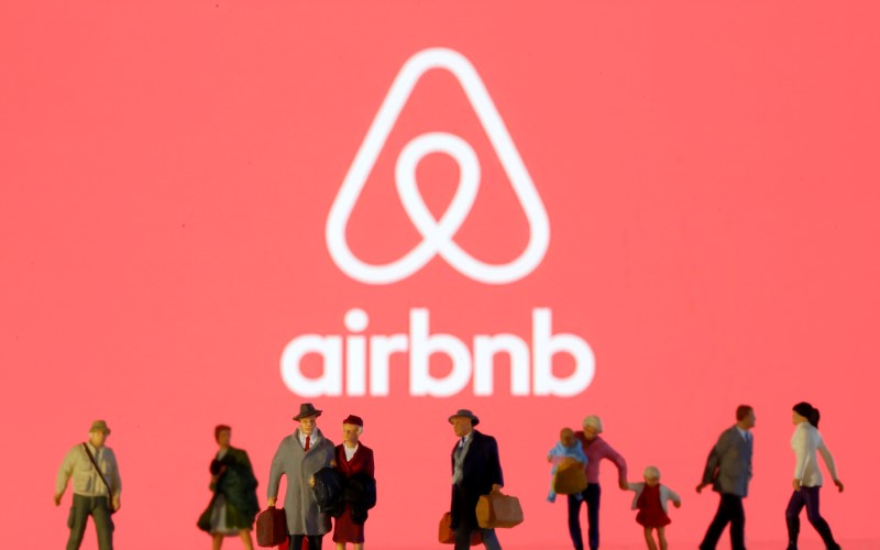 Small toy figures are seen in front of diplayed Airbnb logo