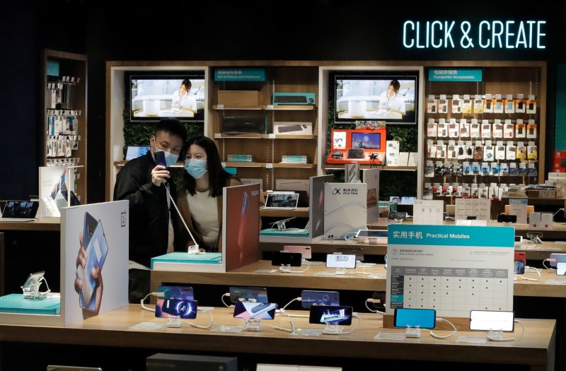 FILE PHOTO: People wearing protective masks look at phones at an electronic retailer in Beijing
