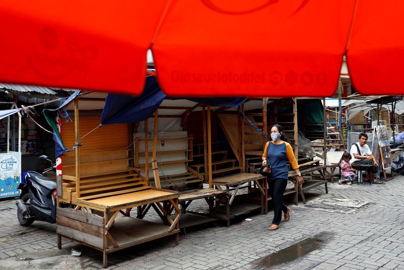 A woman wearing a protective face mask walks past closed street vendors booths at a traditional market amid the spread of the coronavirus disease (COVID-19) in Jakarta
