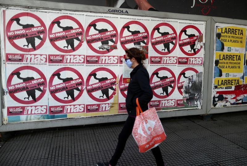 FILE PHOTO: A pedestrian wearing a protective face mask walks past posters on the street that read