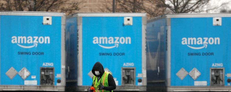 A worker in a face mask walks by trucks parked at an Amazon facility as the global coronavirus outbreak continued in Bethpage on Long Island in New York