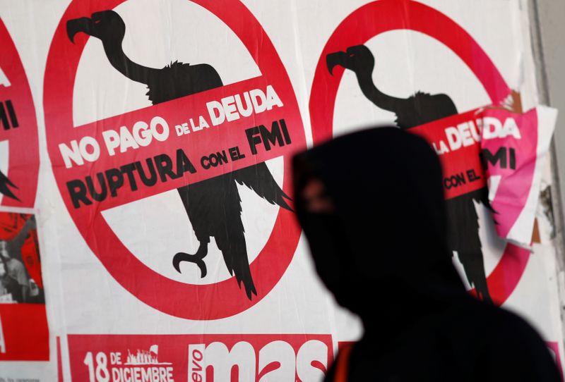A pedestrian wearing a face mask walks past posters on the street that read